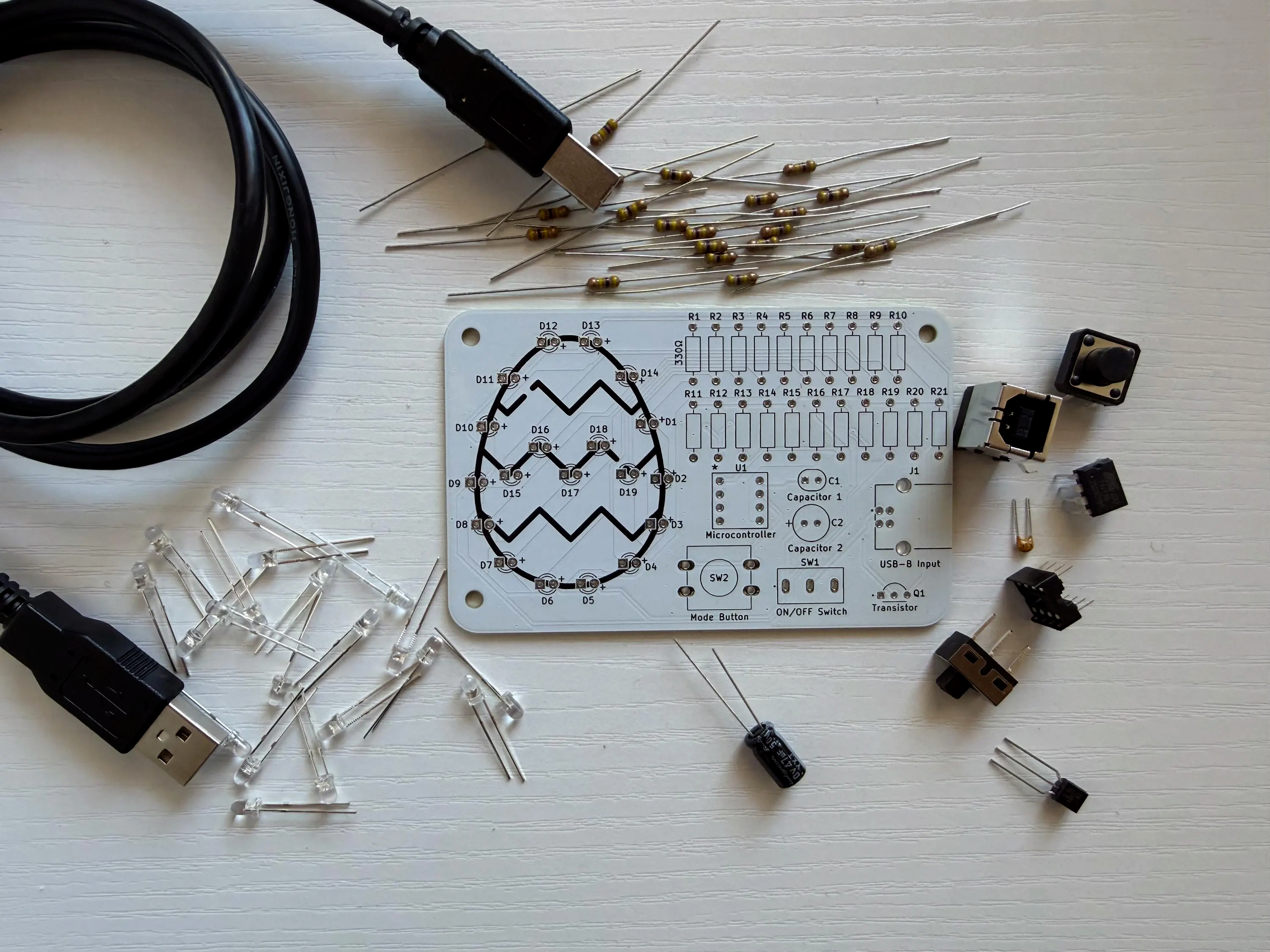 Easter Egg Soldering Kit components laid out flat: PCB, resistors, LEDs, USB cable, buttons